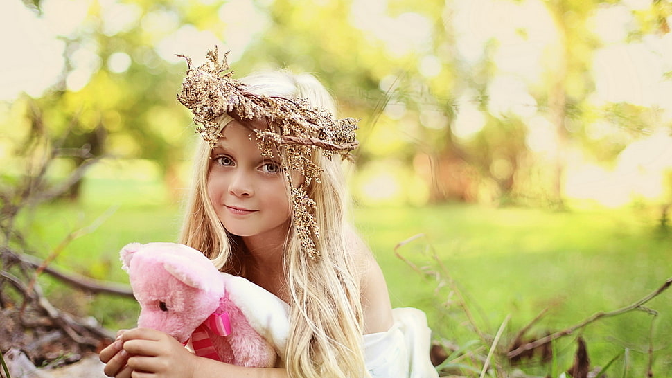 selective focus photography of a girl wearing white top and brown headdress while hugging pink bear plush toy HD wallpaper